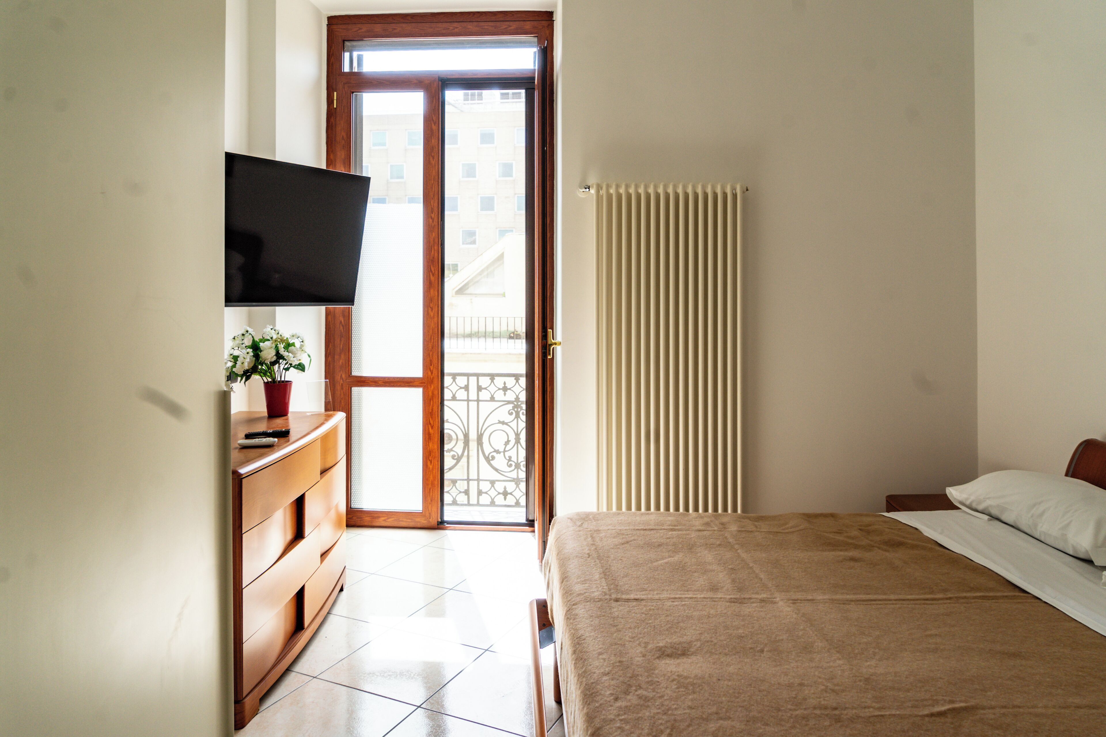 Un dormitorio con una cama, un televisor montado en la pared, un aparador y una planta en maceta.