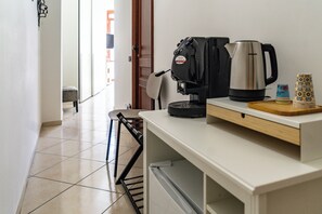 A kitchenette with a coffee maker, a kettle, and a stack of plates on a counter.