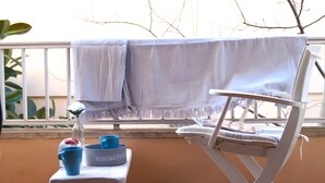 Ein Balkon mit einem weißen Stuhl, einem kleinen Tisch mit einer Schüssel und Tassen sowie einem über den Stuhl geworfenen Handtuch.