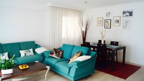 Ein blaugrünes Sofa mit Ziertekissen, ein Couchtisch aus Holz und ein Essbereich mit Stühlen und Tisch.