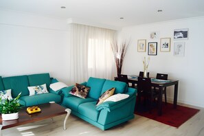 En tealfarvet sofa med dekorative puder, et træbord og et spiseområde med stole og et bord.