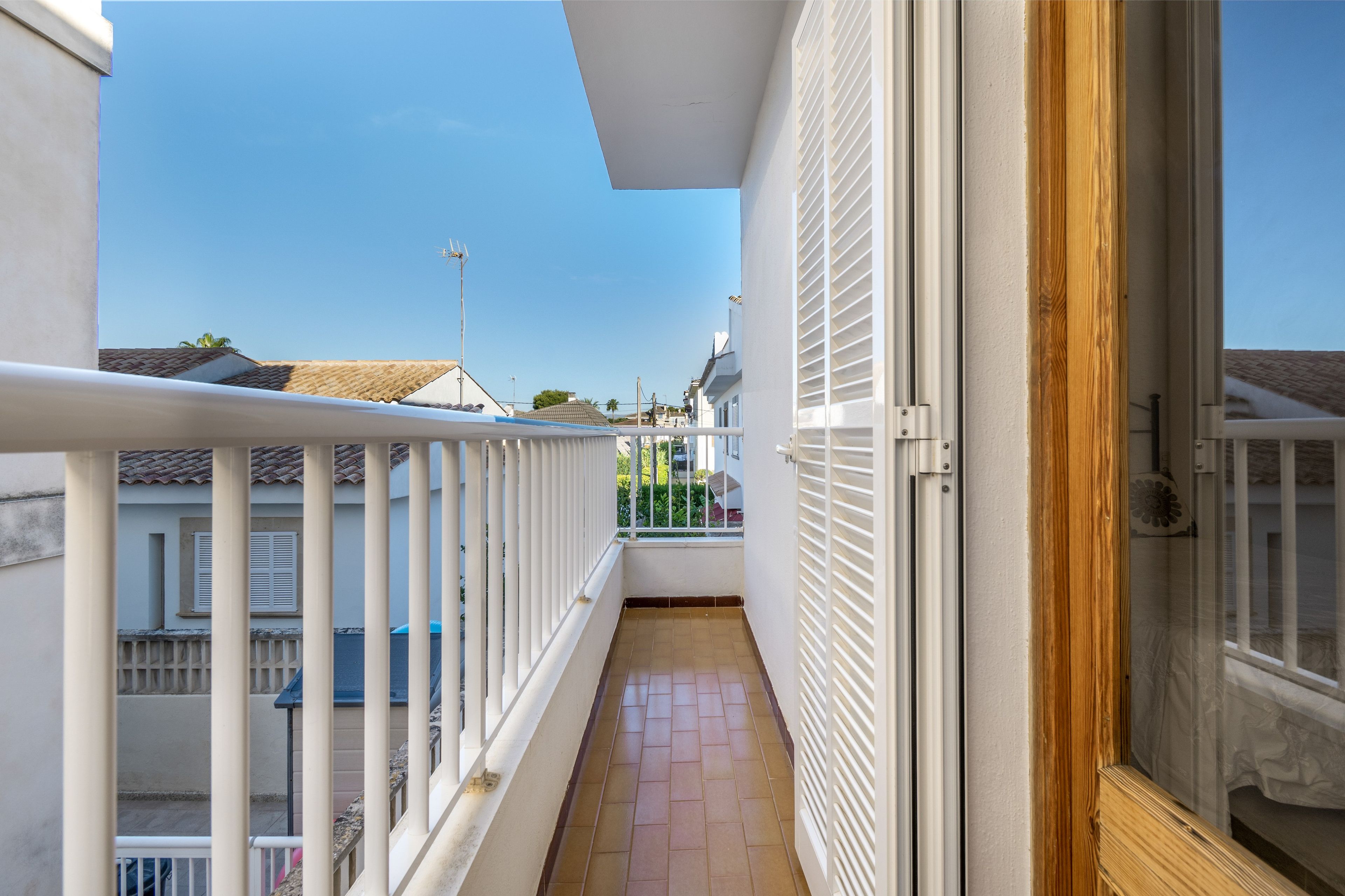 A narrow balcony with a tiled floor, white railings, and a wooden door.
