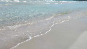 Ein Strand mit klarem Wasser, sanften Wellen und Bergen im Hintergrund.