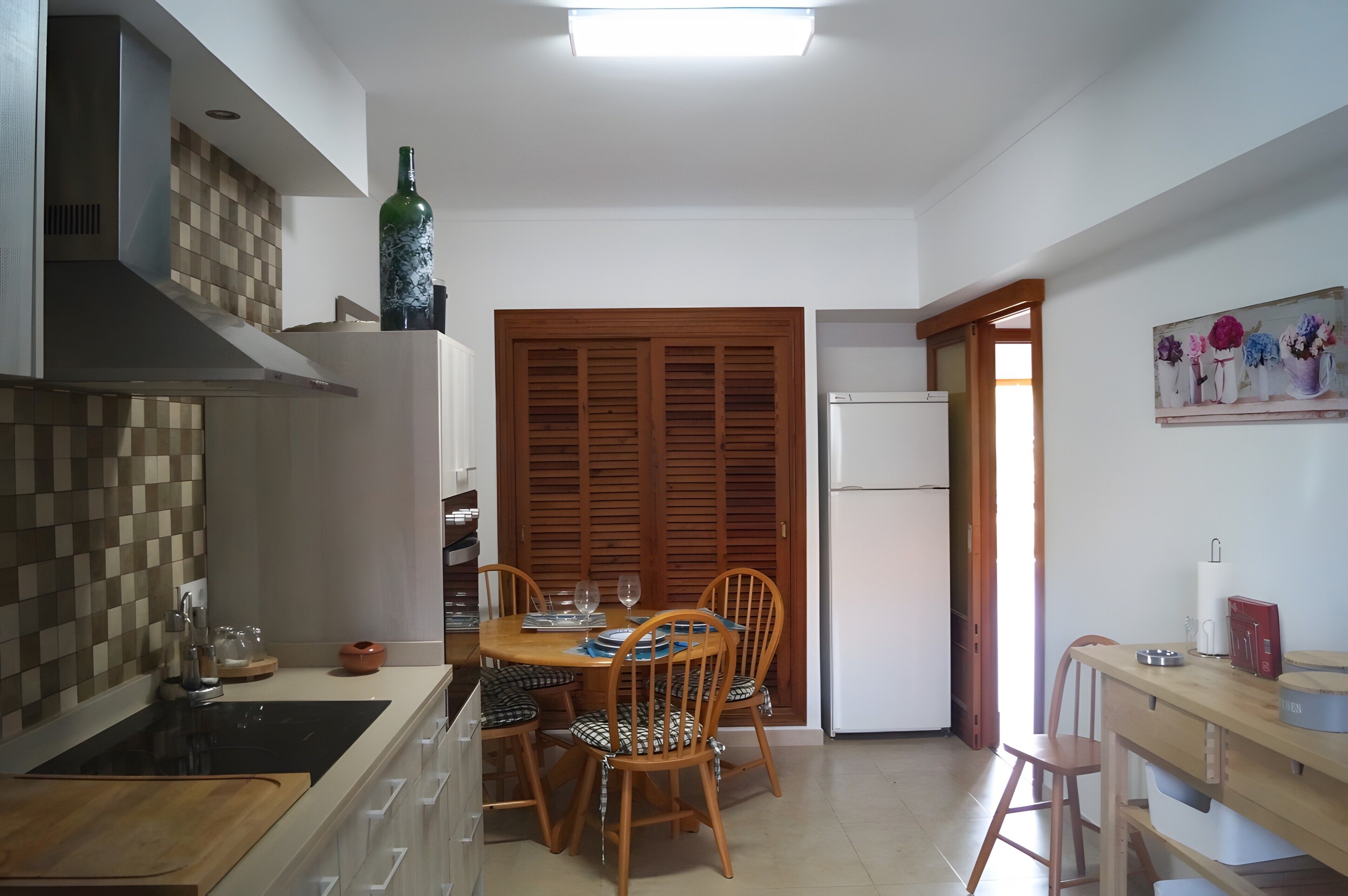 Een compacte keuken met een eethoek, met een houten tafel, stoelen en een koelkast.