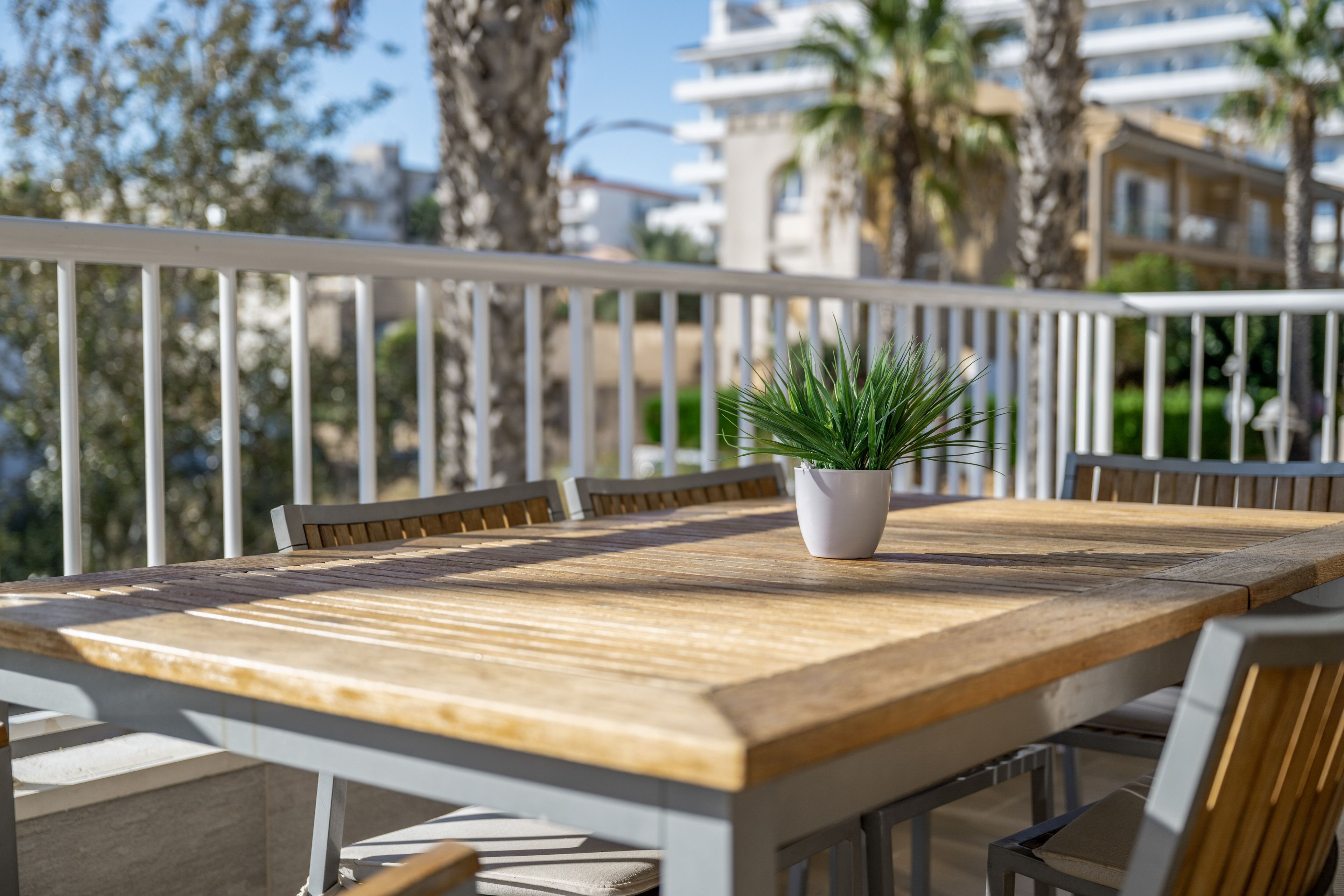 A wooden table with chairs and a potted plant on an outdoor balcony with a white railing.