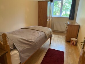 A bedroom with a bed, a radiator, a wardrobe, and a window with a view of trees. - 6 Riverfalls Clifden (Clifden)