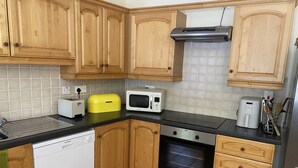 Uma cozinha compacta com armários de madeira, micro-ondas, torradeira e lava-louças.