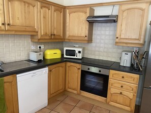 A compact kitchen with wooden cabinets, a microwave, a toaster, and a dishwasher. - 6 Riverfalls Clifden (Clifden)