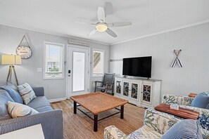 A living room with a ceiling fan, a television, and a cabinet with glass doors. - Oceanfront Condo – And We Truly Mean Oceanfront! (Ocean Isle Beach)