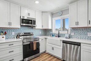 A modern kitchen with white cabinets, a stainless steel microwave, double ovens, and a dishwasher. - Oceanfront Condo – And We Truly Mean Oceanfront! (Ocean Isle Beach)