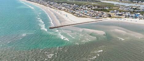 An aerial view of a coastal area with a beach, a pier, and residential buildings.