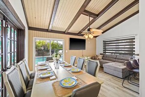 A dining area with a long table, chairs, and a television mounted on the wall. - Fancy Tampa Retreat/Disney/Heated Pool/Clearwater (Tampa)