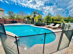 A swimming pool with a curved edge, surrounded by a fence, and equipped with lounge chairs. - Fancy Tampa Retreat/Disney/Heated Pool/Clearwater (Tampa)