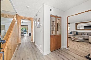 Een modern interieur met een houten trap, een zithoek met een bank en voetenbankje, en een eethoek met een tafel en stoelen.