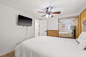 A bedroom with a bed, a ceiling fan, a TV mounted on the wall, and a wooden door. - Fancy Tampa Retreat/Disney/Heated Pool/Clearwater (Tampa)