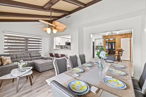 Een moderne woonkamer met een hoekbank, een eettafel gedekt voor zes personen en een keuken op de achtergrond.