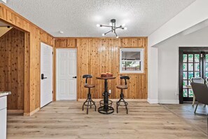A room with wooden panel walls, a white door, a dining table with four chairs, and a ceiling light fixture. - Fancy Tampa Retreat/Disney/Heated Pool/Clearwater (Tampa)