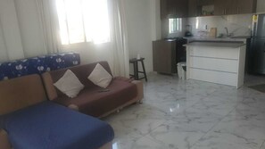 Ein Wohnzimmer mit einer Couch, einem kleinen Tisch und einer Küchenzeile mit Kühlschrank und Spüle.
