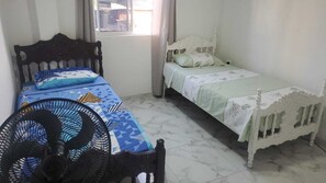 A room with two beds, one with a patterned bedspread and the other with a plain one. There is a standing fan in the foreground. - Enjoyable 2-bedroom apartment with AC in Cartagena de Indias (Cartagena de Indias)