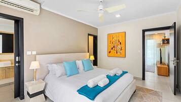 A hotel room with a bed, bedside tables, a ceiling fan, a painting, and a door leading to another room.