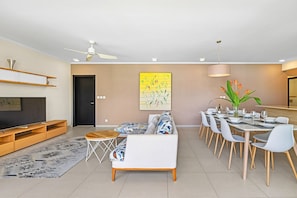 A modern living room with a sofa, coffee table, and dining area with chairs and a table set for a meal. - 17 Ocean Legend (Tamarin)