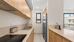 Una cocina moderna con armarios de madera, un lavamanos de acero inoxidable y una placa de cocción por inducción negra.