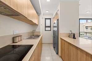 A modern kitchen with wooden cabinets, a stainless steel sink, and a black induction cooktop. - 17 Ocean Legend (Tamarin)