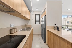 Una cocina moderna con armarios de madera, un lavamanos de acero inoxidable y una placa de cocción por inducción negra.