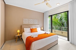 A hotel room with a bed, nightstands, a ceiling fan, and a view of greenery through large windows. - 17 Ocean Legend (Tamarin)