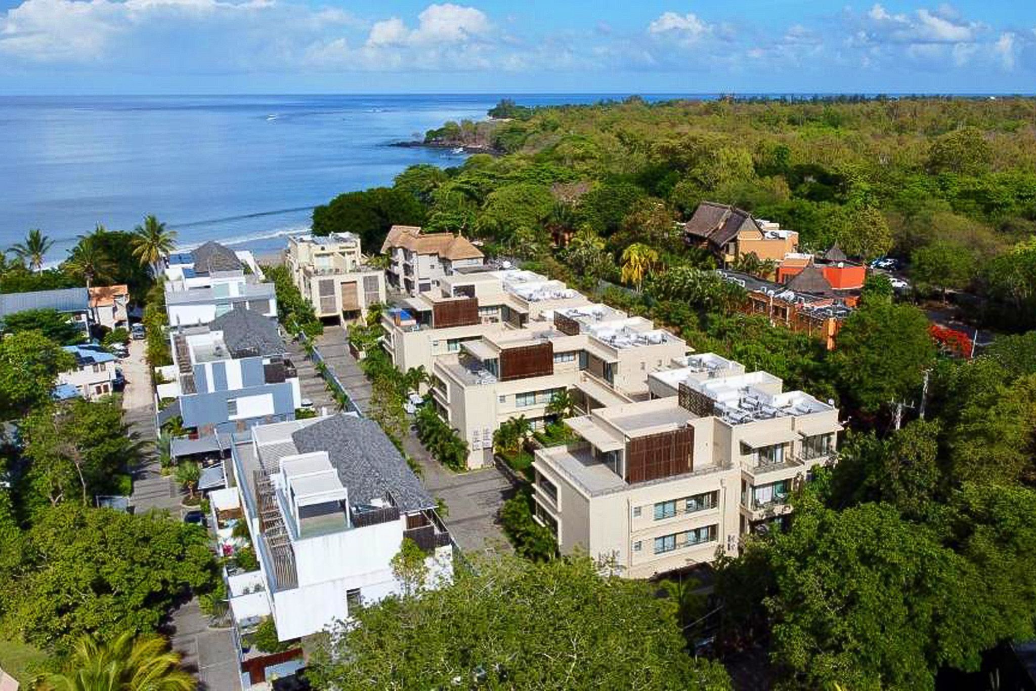 Un quartier résidentiel en bord de mer, avec des bâtiments modernes, une vue dégagée sur l’océan et une végétation luxuriante.