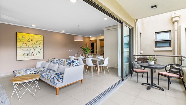 Una sala de estar moderna con sofá, mesa de comedor y sillas. Se ve una cocina a través de una puerta abierta.
