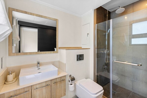 Un baño moderno con cabina de ducha de vidrio, un lavamanos blanco y un espejo con marco de madera.