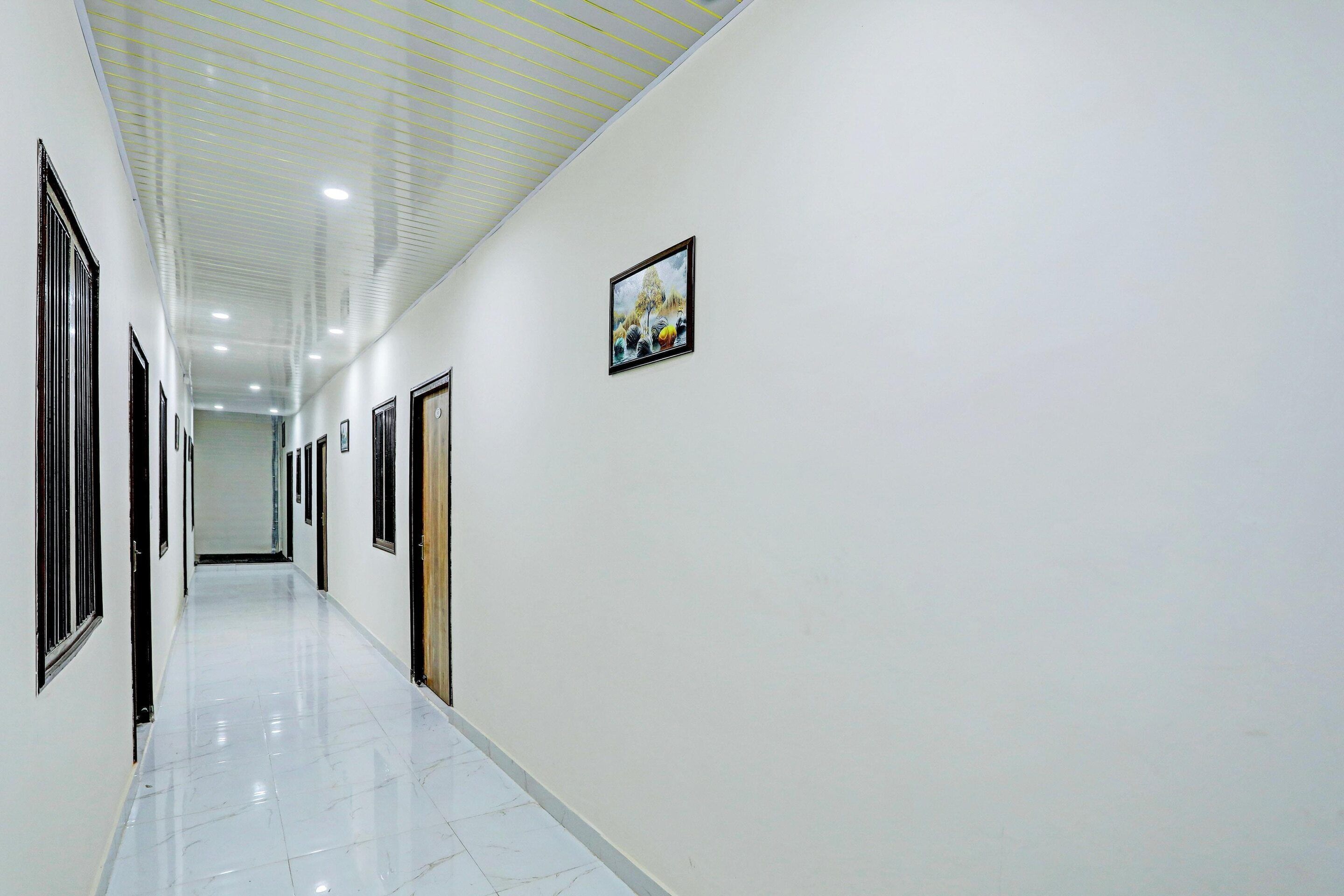 A long, narrow hallway with white walls and doors, leading to a room at the end.