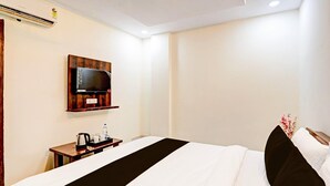 A hotel room with a bed, a television mounted on the wall, a small table with a kettle and cups, and a power outlet. - Deluxe Lucknow Inn (Lucknow)