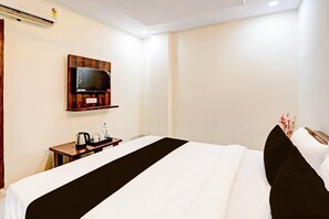 A hotel room with a bed, a television mounted on the wall, a small table with a kettle and cups, and a power outlet. - Deluxe Lucknow Inn (Lucknow)
