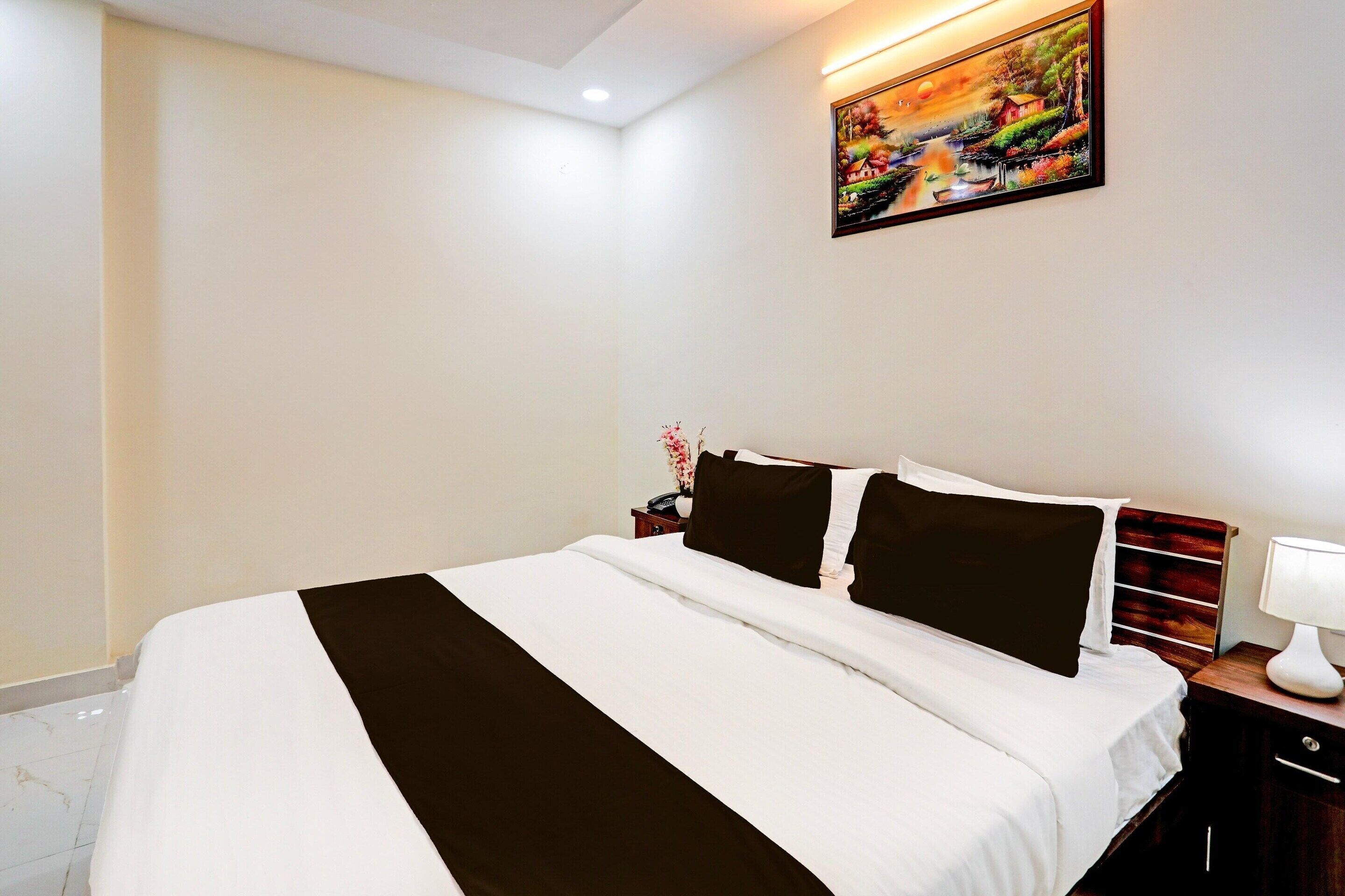 A hotel room with a bed, a nightstand, a lamp, and a painting on the wall.