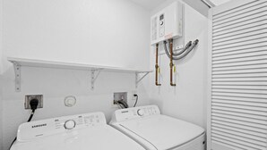 A laundry room with two white front-loading washers and dryers, a control panel above the dryers, and a vent system on the wall. - Cozy Haven (Miami)