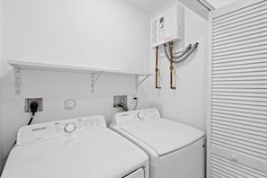 A laundry room with two white front-loading washers and dryers, a control panel above the dryers, and a vent system on the wall. - Cozy Haven (Miami)