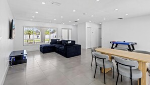 A modern living room with a sectional sofa, a dining table with chairs, and a pool table. - Cozy Haven (Miami)
