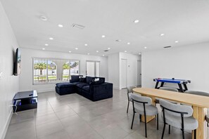 A modern living room with a sectional sofa, a dining table with chairs, and a pool table. - Cozy Haven (Miami)