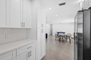 A modern kitchen with white cabinets, a stainless steel refrigerator, and a dining area with a table and chairs.