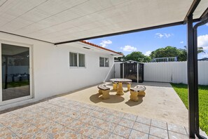 A covered patio area with a tiled floor, a small round table, and two chairs. - Cozy Haven (Miami)
