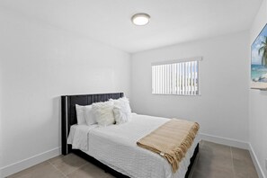 A bedroom with a bed, a window with blinds, and a ceiling light.