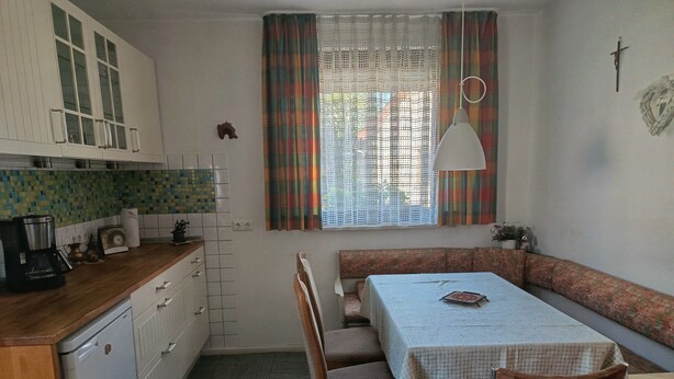 A compact kitchen with a dining area, featuring a bench, chairs, a table, and a window with curtains.