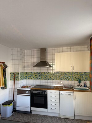 Una cocina con armarios blancos, estufa, lavavajillas y salpicadero de azulejos.
