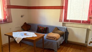 A room with a wooden floor, a sofa with cushions, a table with a white cloth, and a window with curtains.
