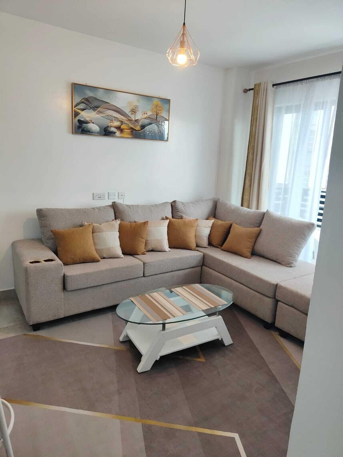 A living room with a sectional sofa, a glass coffee table, a painting on the wall, and a window with curtains.