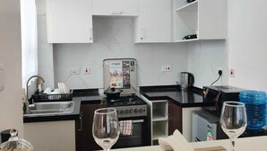 A modern kitchen with white cabinets, a stove, and a microwave. There are two wine glasses on the counter. - The Enkang Urban Escape (Nairobi)