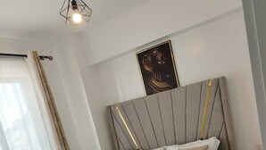 A modern bedroom with a large bed, a headboard with gold accents, a bedside table, and a wall-mounted artwork. - The Enkang Urban Escape (Nairobi)