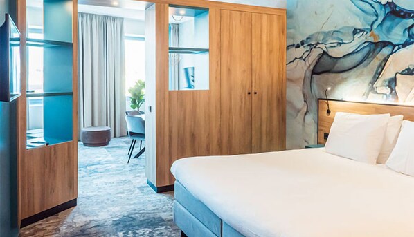 Hotellihuone, jossa on sänky, työpöytä, tuoli, vaatekaappi ja taulu seinällä.